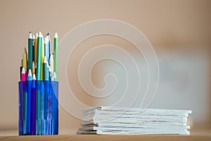 Wooden colorful drawing pencils arranged in plastic jug and stack of copybooks on light copy space background