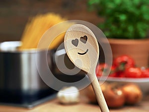 wooden cooking spoon with heart smiley in front of saucepan with spaghetti and other ingredients