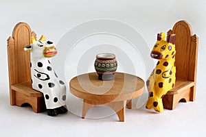 Wooden cow and cheetah are sitting on chairs near the table. Closeup