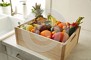 Wooden crate with assortment of exotic fruits on table in kitchen