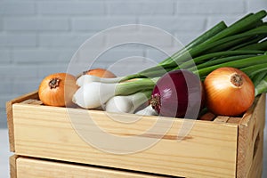 Wooden crate with different kinds of onions near white brick wall, closeup