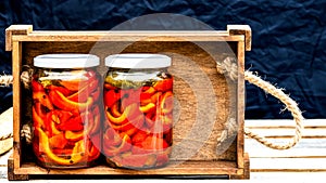 Wooden crate with glass jars with pickled red bell peppers.Preserved food concept, canned vegetables isolated in a rustic