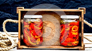 Wooden crate with glass jars with pickled red bell peppers.Preserved food concept, canned vegetables isolated in a rustic