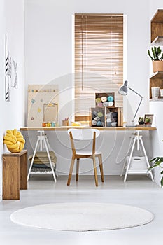 Wooden crates with dark and colorful yarn and other sewing tools on a wide workspace desk in a bright crafts room interior. Real p