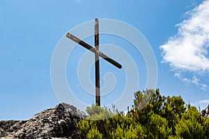 Wooden cross atop the peak of a rocky mountain against the cloudy blue sky