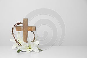 Wooden cross, crown of thorns and blossom lilies on table against light background photo
