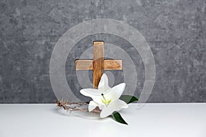 Wooden cross, crown of thorns and blossom lily on table