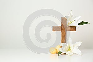 Wooden cross, Easter eggs and blossom lilies on table against light background