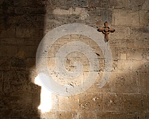 Wooden cross hanging on an old stone wall in a church, partially lit with sun rays