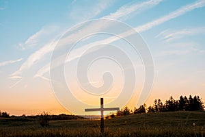 Wooden cross in the middle of a grassy field under a blue sky