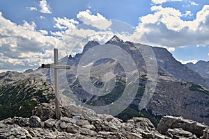 Wooden cross on a mountain peak with mountains under blue sky and white clouds in the background
