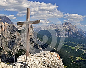 Wooden cross on a mountain peak with mountains, valley with forest and blue sky with white clouds in the background