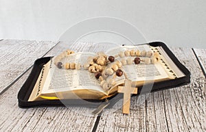 the wooden cross over opened bible on wooden table with window light, vintage tone