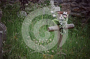 Wooden cross with plastic flowers among the grass