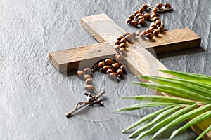 Wooden cross, rosary and palm on black marble background, palm sunday concept