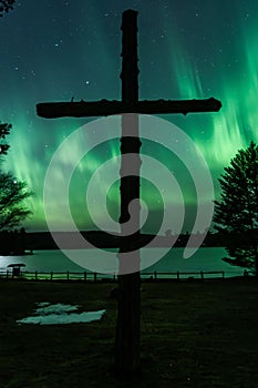 Wooden cross is situated on the side of a road, with northern lights in the background