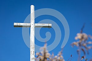 Wooden cross stands against a vivid blue sky with a blossoming tree in the foreground
