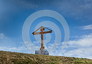 Wooden cross stands on a hill on a background of sky.