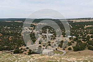 Wooden cross on a stone with green tree land in the background under a cloudy blue sky