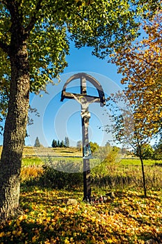 Drevený kríž obklopený bujnými stromami. Kostol sv. Jána Krstiteľa, Kremnické Bane, Slovensko.