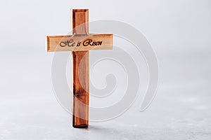 Wooden cross with text He is risen on grey background. Reminder of Jesus sacrifice and Christ resurrection. Easter passover.