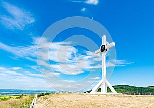 A wooden cross on top of a hill. Orthodox white cross glows on the top of the hill on the background of blue sky and of green gras