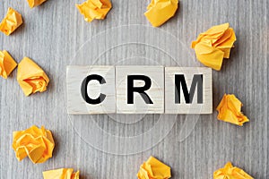 Wooden cube with CRM text Customer Relationship Management and crumbled paper on table background. Financial, marketing and