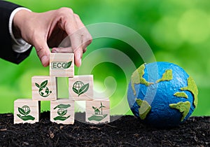 Wooden cube with eco symbol and paper globe on fertile soil background. Alter