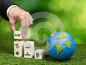 Wooden cube with eco symbol and paper globe on fertile soil background. Alter