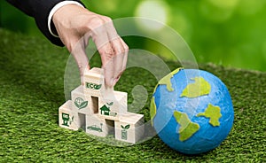 Wooden cube with eco symbol and paper globe on fertile soil background. Alter