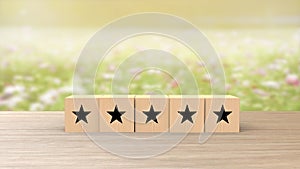 Wooden cube five black star review on blur field of flowers background. Service rating, satisfaction concept. reviews and comments