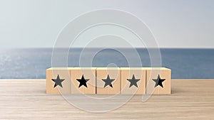 Wooden cube five black star review on blur sea with the sky background. Service rating, satisfaction concept. reviews and comments