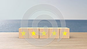 Wooden cube five yellow star review on blur sea with the sky background. Service rating, satisfaction concept. reviews and