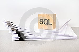 a wooden cube with a text SQL on a stack of documents. grey table, white background