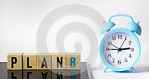 Wooden cube with the word PLAN B on a black and white background with a clock. business concept