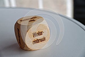 Wooden cube with words winter einbruch winter onset in german on plain surface