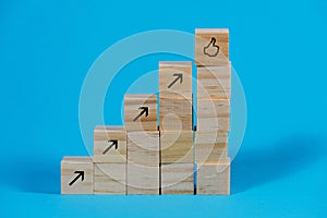 Wooden cubes arranged as stair steps with arrows pointing upwards and a thumb up symbol on the top, business growth and management