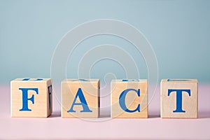 Wooden cubes with blue letters with word fact on pink and gray background with free space for text. False and real fact