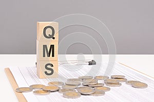 wooden cubes on a brown background with the text QMS - an abbreviation for Quality Management System. strong business