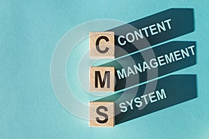 Wooden cubes building word CMS - abbreviation content management system on light blue background