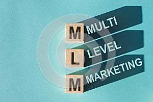Wooden cubes building word MLM - multi level marketing, on light blue background