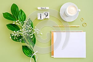 Wooden cubes calendar March 19. Notepad, cup of coffee, bouquet flowers on green background. Concept hello spring Top view Flat