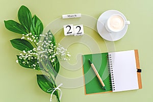 Wooden cubes calendar March 22. Notepad, cup of coffee, bouquet flowers on green background. Concept hello spring Top view Flat