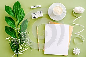 Wooden cubes calendar March 27. Notepad, cup of coffee, bouquet flowers on green background. Concept hello spring Top view Flat