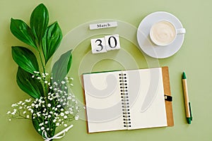 Wooden cubes calendar March 30. Notepad, cup of coffee, bouquet flowers on green background. Concept hello spring Top view Flat