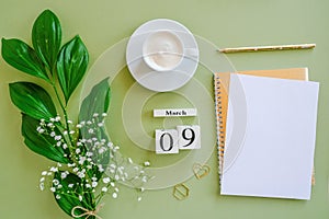 Wooden cubes calendar March 9. Open blank notepad, cup of coffee, bouquet flowers on green background. Concept hello