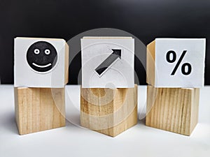 Wooden cubes in a column and a row with white signs with a smiley sign, an arrow, a percentage. The concept of