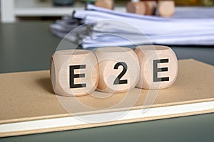 Wooden cubes with E2E letters on notebook, symbolizing end-to-end business process.
