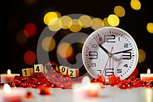 Wooden cubes on February 14, Valentine`s day. White clock on table among red glass hearts and candles