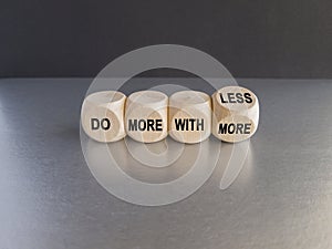 Wooden cubes form the expression \'do more with less\'. Beautiful grey table, black background.